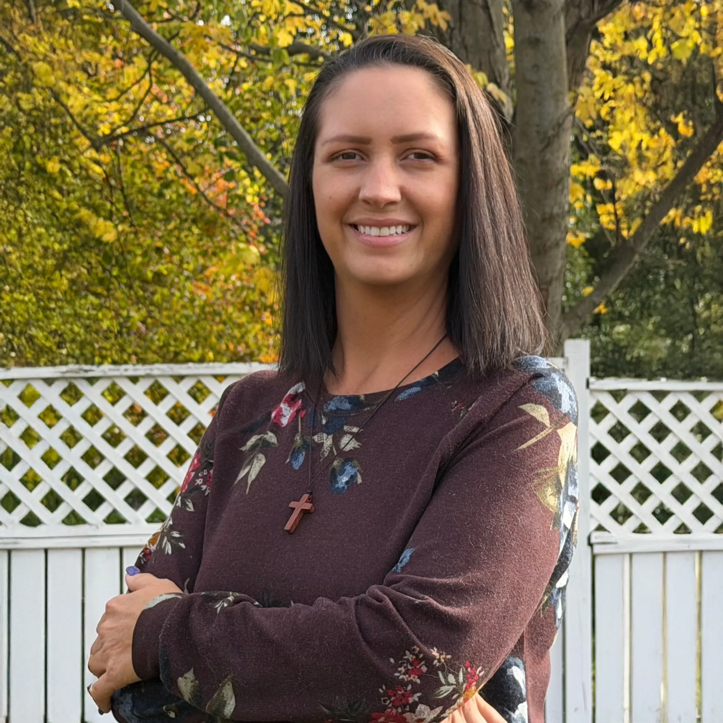 Rhonda Redd, a woman with long dark hair smiling in a floral top, standing outdoors with autumn trees in the background
