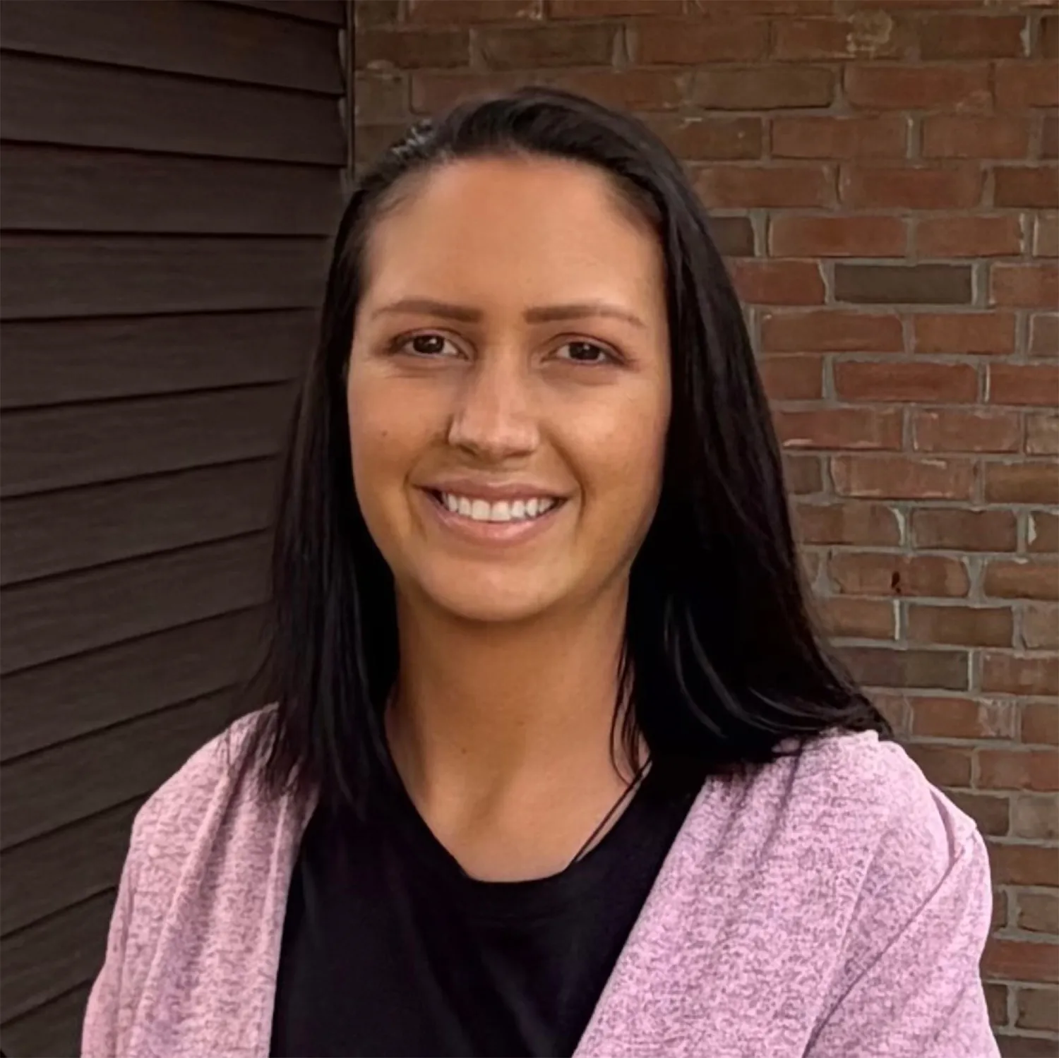 Rhonda Redd, a woman with long dark hair smiling in a light purple cardigan, photographed against a brick wall